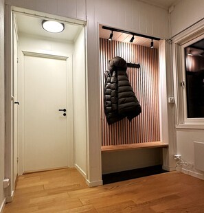 A hallway with a white door, a bench with a coat rack, and a wooden slatted wall. - Sentrumsnær leilighet med 4 soverom - Aurora (Tromsø)