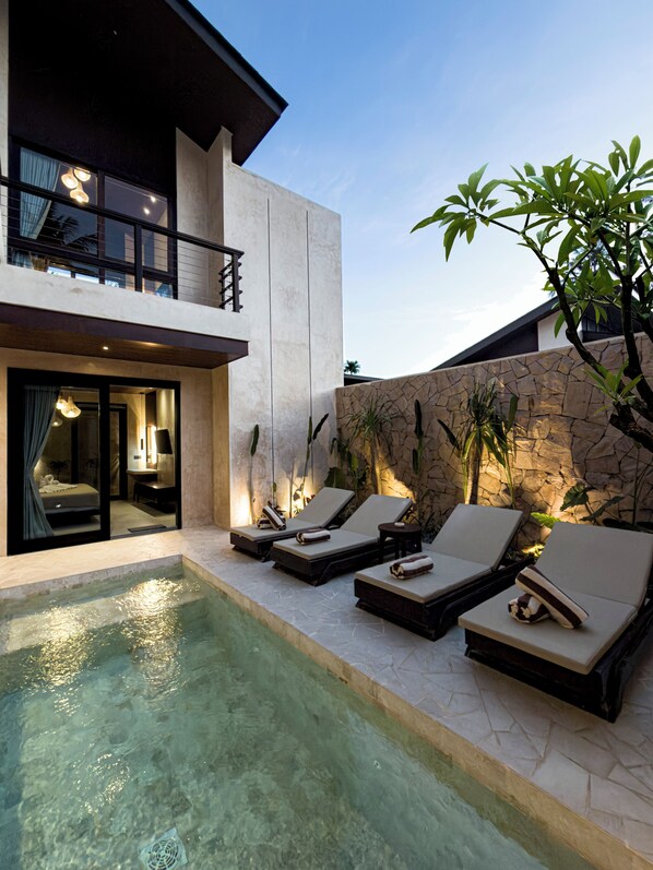A modern house with a swimming pool, lounge chairs, and a stone wall.