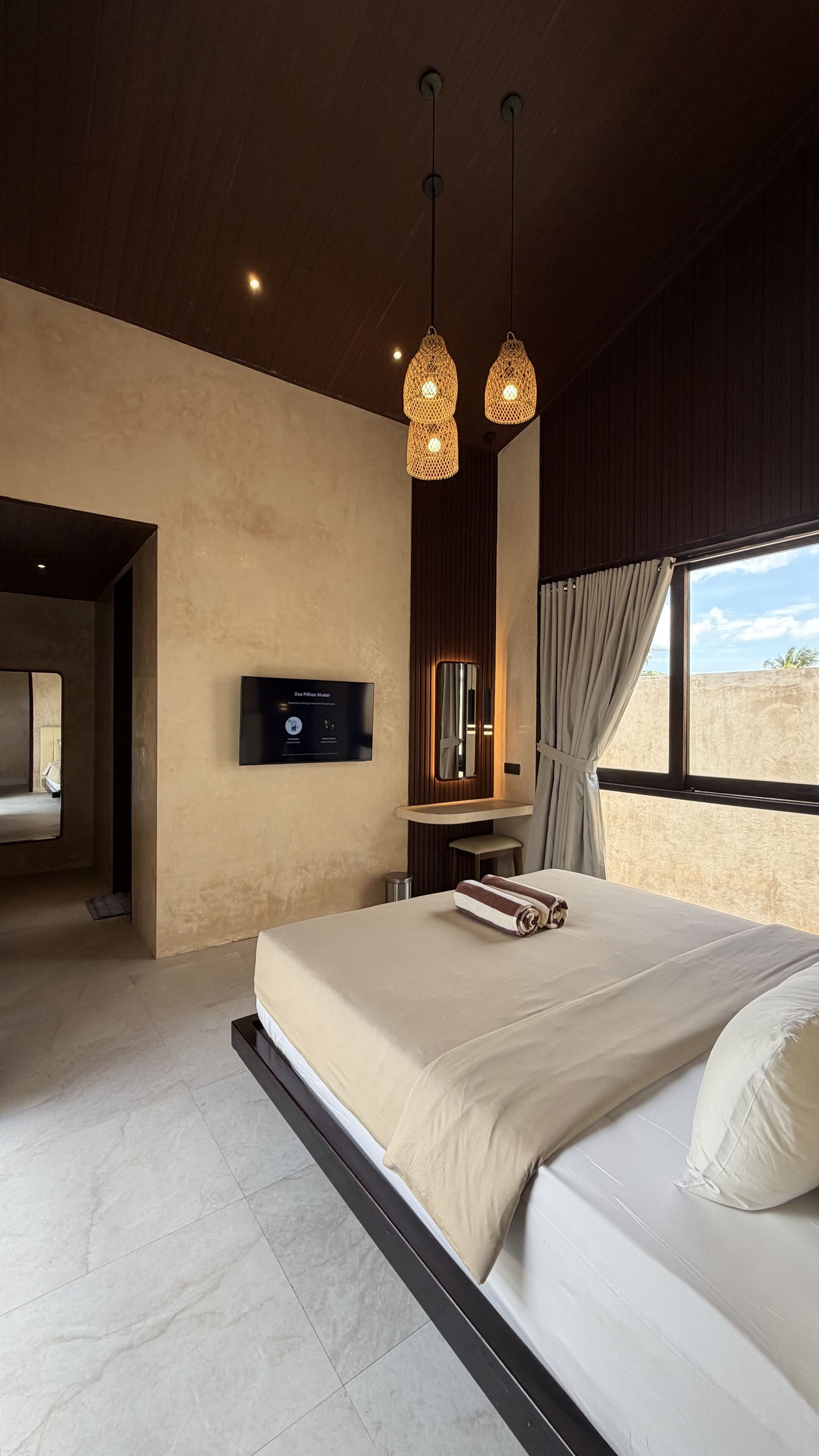 Ein modernes Schlafzimmer mit einem großen Bett, einem an der Wand befestigten Fernseher und einem Fenster mit Vorhängen.