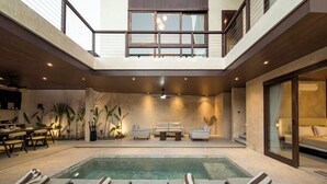 Et moderne poolområde indendørs med liggestole, et spiseområde og en trappe til et øvre niveau.