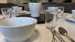A modern kitchen with white cabinets, a central island with a white bowl and a potted plant, and a dining area with a white table set for two. - Sentral leilighet med 3 soverom og kjøkken - Mare (Tromsø)
