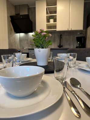 Eine moderne Küche mit weißen Schränken, einer zentralen Kochinsel mit einer weißen Schüssel und einem Blumentopf, sowie ein Essbereich mit einem weißen Tisch für zwei Personen.
