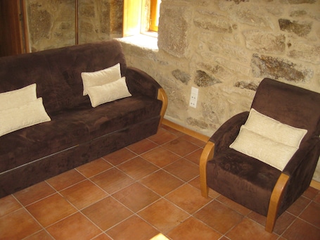 A room with a stone wall, a brown sofa with cushions, and a wooden chair.. Fabulous 2-bedroom House in a Portuguese traditional mountain village
