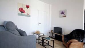 A living room with a grey sofa, a brown leather chair, a small table with a basket, and a TV stand. - Le Logis de Lucie ( 6 people) (Lys-Haut-Layon)