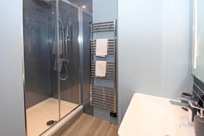 A modern bathroom with a glass shower enclosure, a towel rack, and a white sink. - St John's Hill Apartments (Shrewsbury)