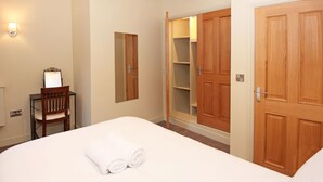 A hotel room with a bed, a chair, a desk with a mirror, and wooden wardrobes.