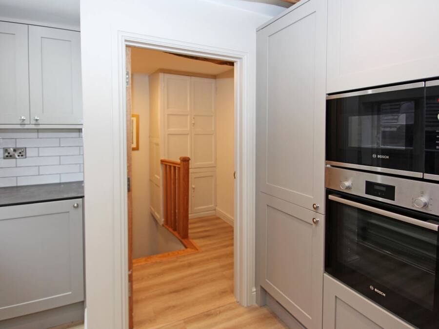 A kitchen with white cabinets, a Bosch oven, and a wooden staircase leading to another room.