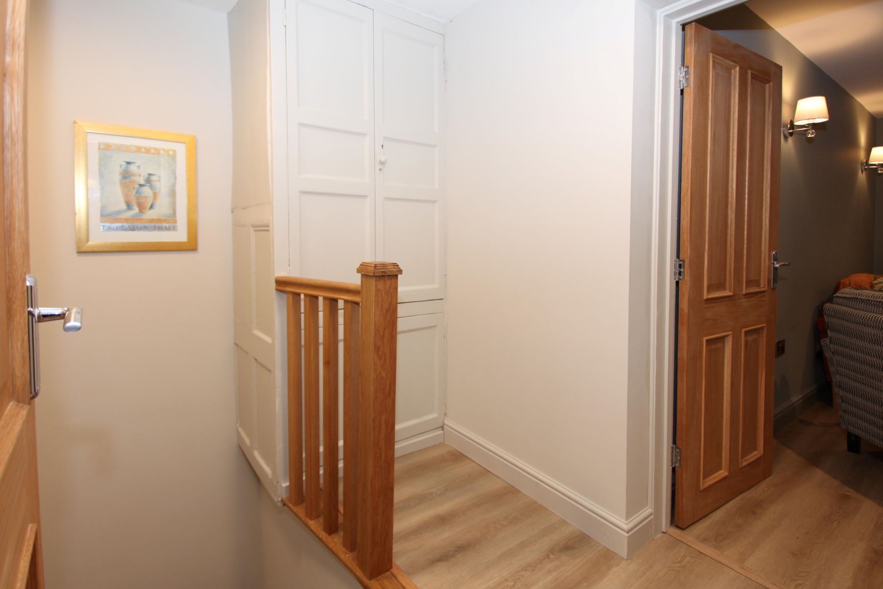 A hallway with a wooden staircase, white doors, and a framed picture on the wall.