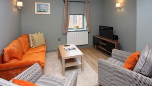 A living room with a sofa, armchairs, a coffee table, a TV, and a window with curtains.