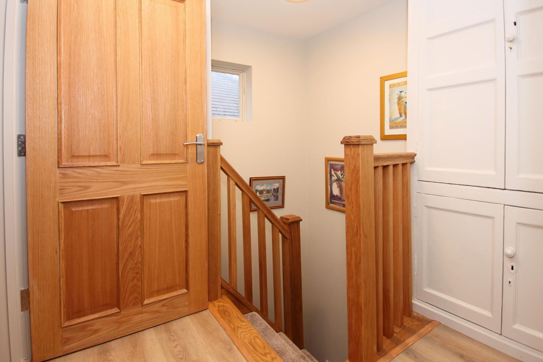 A wooden staircase with a handrail, a door with a handle, and a window with blinds.