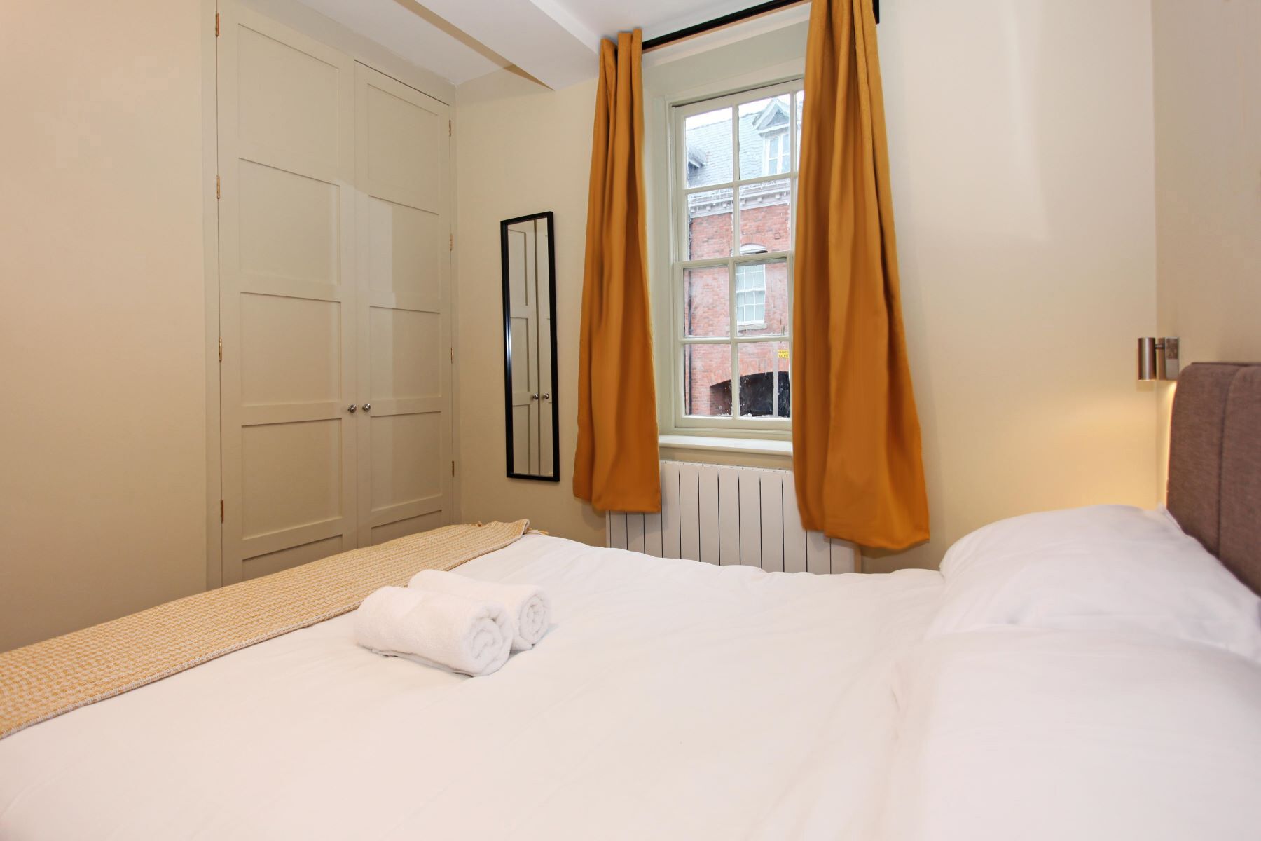 Une chambre d’hôtel avec un lit, une fenêtre avec des rideaux, un radiateur et une armoire.