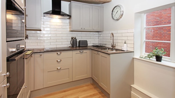 A kitchen with grey cabinets, a black range hood, a stainless steel sink, and a clock on the wall.