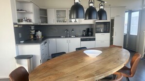 A modern kitchen with white cabinets, a wooden dining table, and three black pendant lights.
