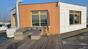 A modern building with a wooden deck, a built-in sofa, and large windows.