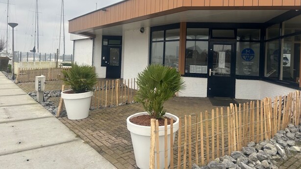 A modern building with a flat roof, large windows, and a wooden fence.