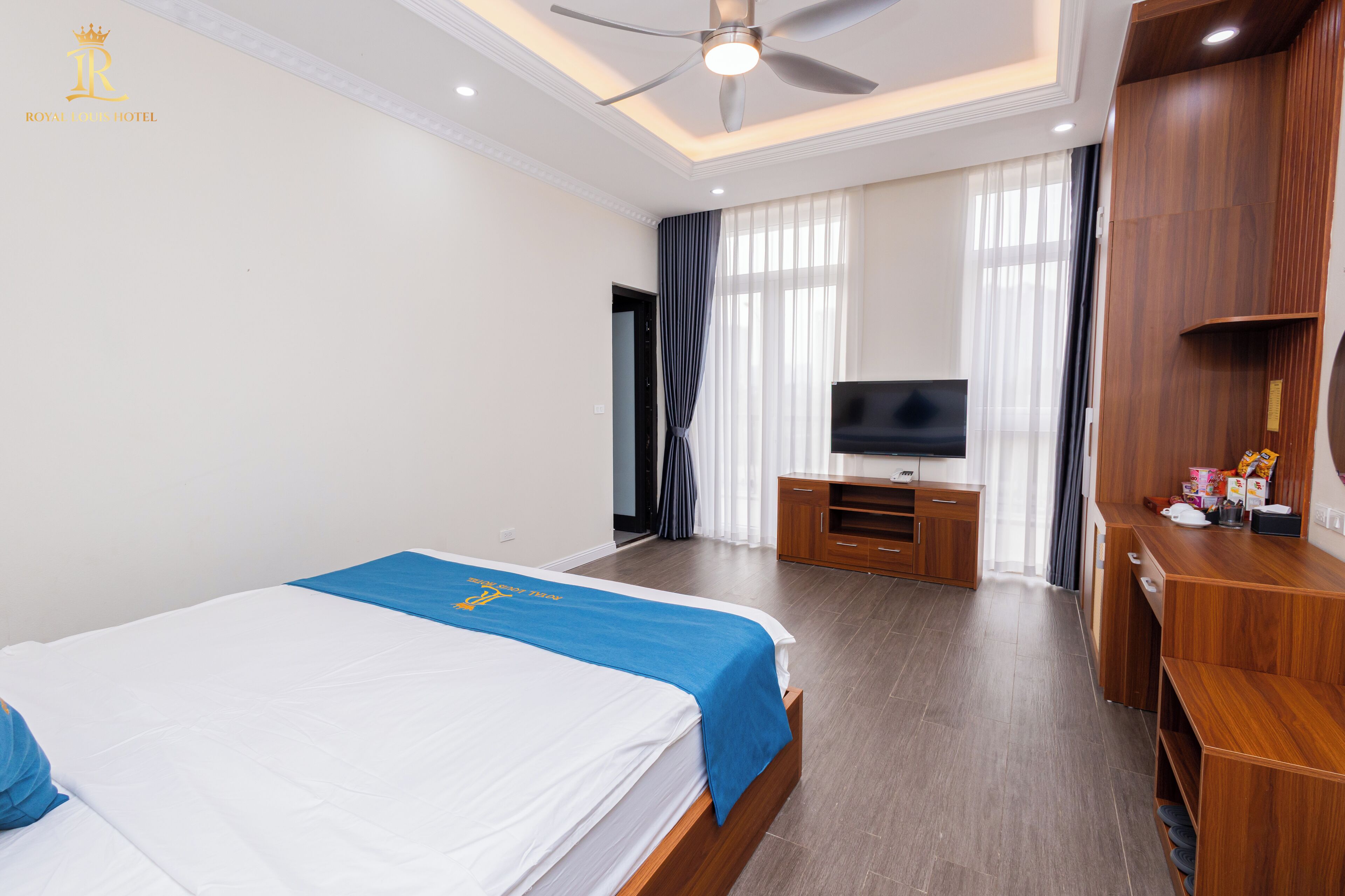 Una habitación de hotel con cama, televisor, muebles de madera y ventilador de techo.