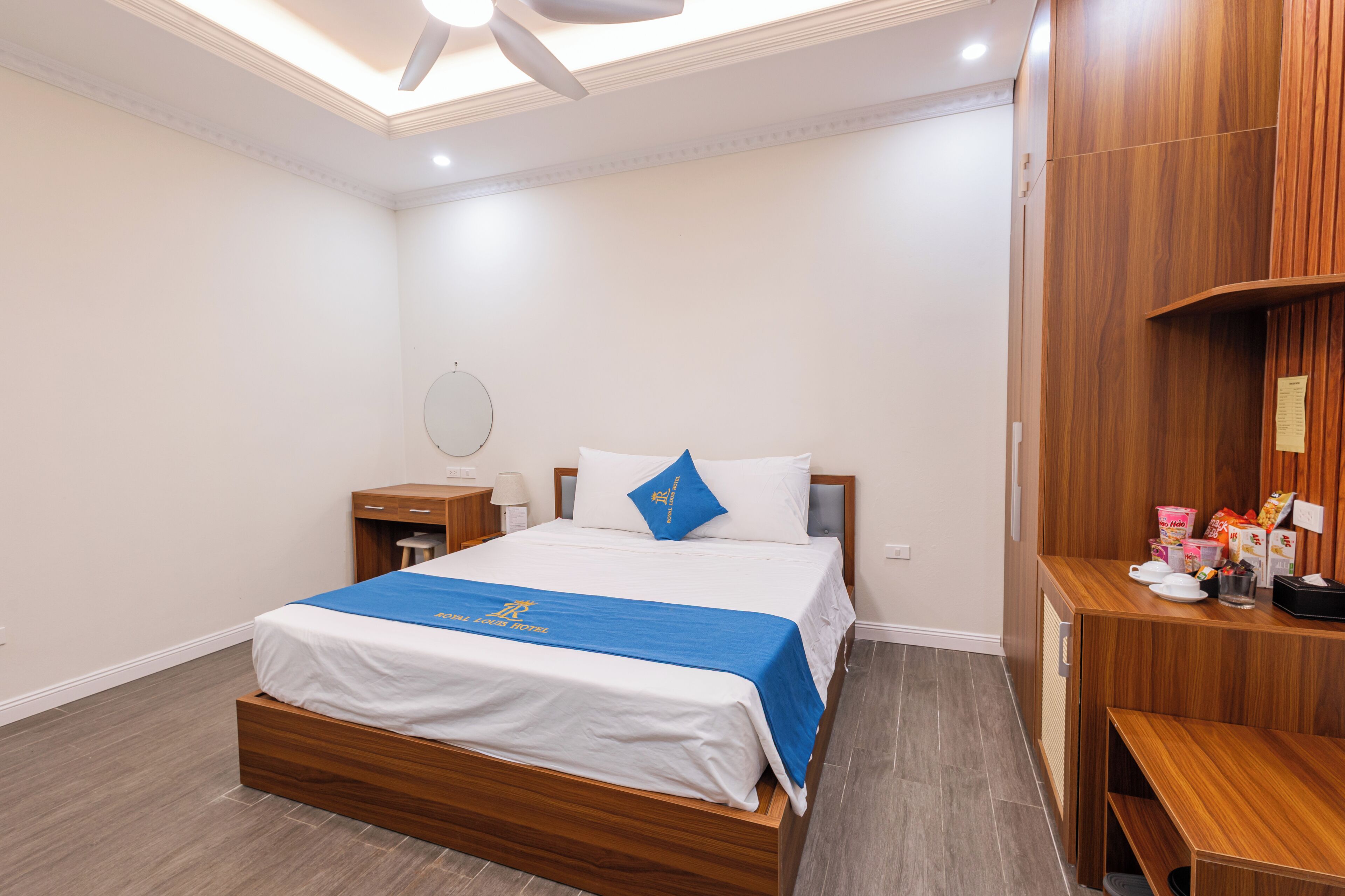 A hotel room with a wooden bed, a bedside table, a nightstand, a desk, and a chair.