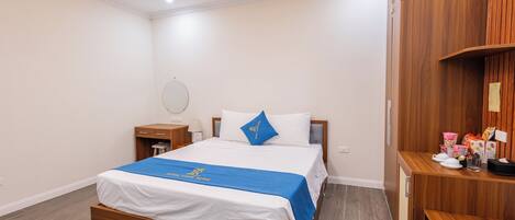 A hotel room with a wooden bed, a bedside table, a nightstand, a desk, and a chair.