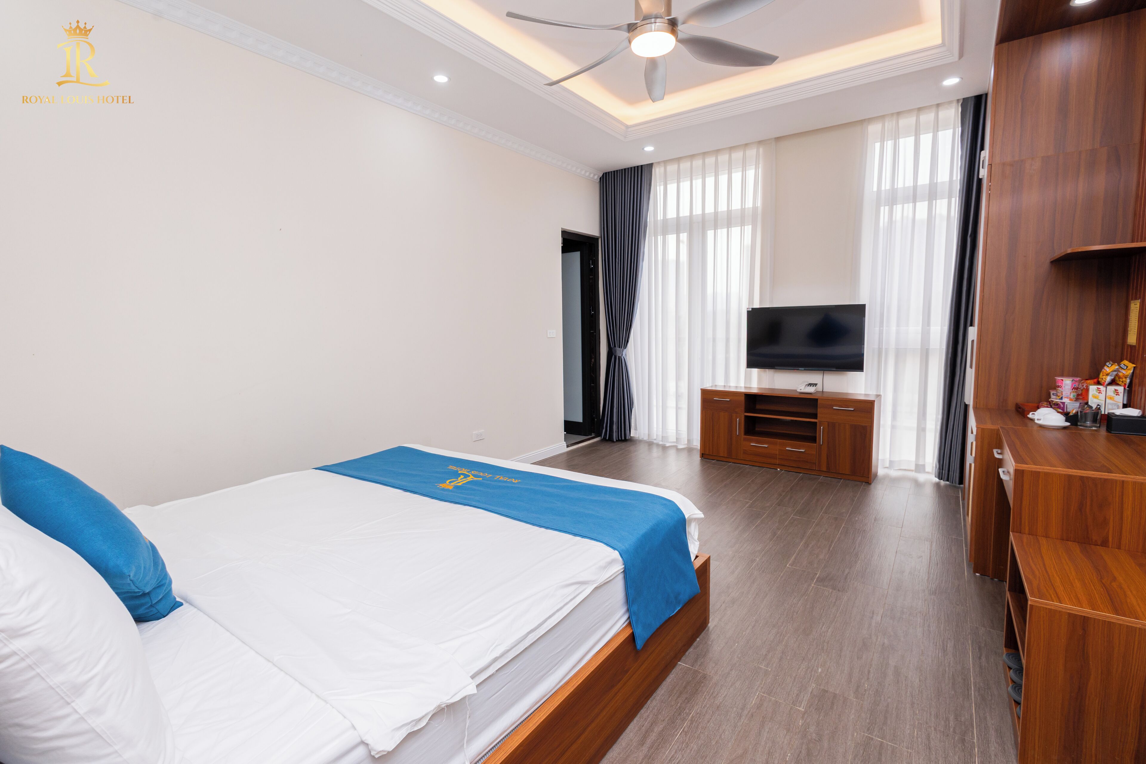 A hotel room with a bed, a TV, a desk, and a ceiling fan.