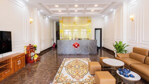 A lobby with a reception desk, a television, a sofa, a coffee table, and a decorative rug. - Royal Louis Hotel (Hanoi)