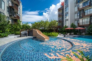 Ein Swimmingpool mit Wasserrutsche, umgeben von Grünflächen und einem mehrstöckigen Gebäude mit Balkonen.