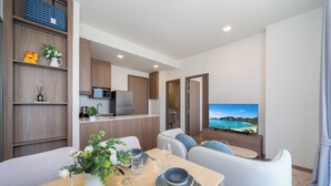 A modern living room with a dining area, a kitchen, and a TV displaying a scenic view. - Canvas Condo New 2BR Near Beach 111-80 (Choeng Thale)