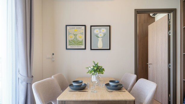 A dining table with four chairs, two framed botanical prints on the wall, and a vase with flowers on the table. - Canvas Condo New 2BR Near Beach 111-80 (Choeng Thale)
