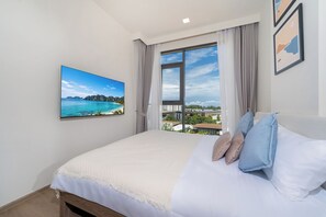 A bedroom with a large bed, a window with a view of buildings, and a framed picture on the wall. - Canvas Condo New 2BR Near Beach 111-80 (Choeng Thale)