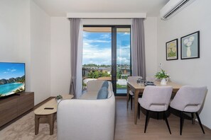 Een moderne woonkamer met een flatscreen televisie, een bank, een eettafel met stoelen en een balkon met uitzicht.