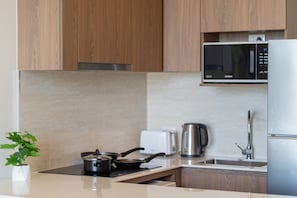A modern kitchen with wooden cabinets, a microwave, a kettle, a toaster, and a sink. - Canvas Condo New 2BR Near Beach 111-80 (Choeng Thale)