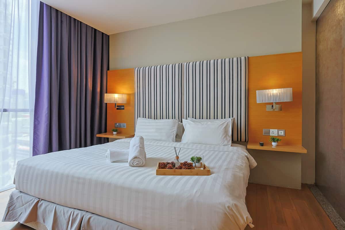 A hotel room with a large bed, two bedside tables, a headboard, and a window with curtains.