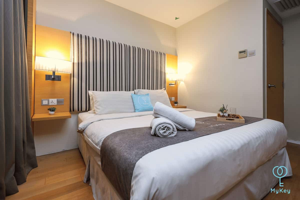 A neatly made bed with a grey and white striped headboard, two bedside lamps, and a small table with a plant and a tray.