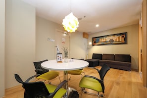 Una habitación moderna con una mesa redonda, sillas verdes y negras, un sofá marrón y una lámpara colgante.