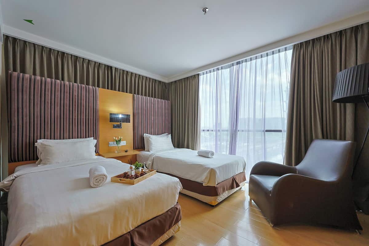 A hotel room with two beds, a chair, a nightstand, and a large window with curtains.