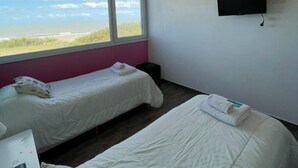 A room with two beds, a TV on the wall, and a window with a view of the beach.