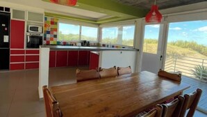 A modern kitchen with red and white cabinetry, a wooden dining table, and a view of the outdoors.