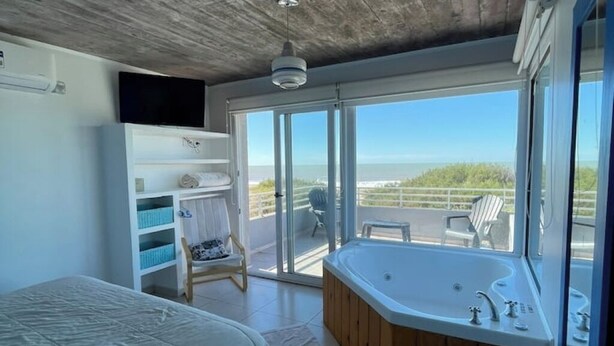Ein Schlafzimmer mit großem Fenster, einer Glasschiebetür, die auf einen Balkon führt, einer Holzwanne und einem an der Wand befestigten Fernseher.
