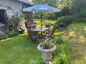 A stone building with a wooden door, a table with chairs, and a blue umbrella. - Our 17th century Barn converted into a relaxed, bohemian home. (Honfleur)