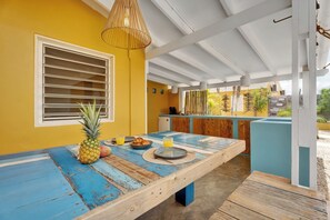 A dining area with a wooden table, a pineapple, and a fruit bowl. - Welcome to Kas Blou, your breezy, blue-accented island escape at Barefoot Apartments in Kralendijk, Bonaire.<br>This cozy one-bedroom studio offers authentic Caribbean charm, great value, and a peaceful location just a short walk from everything. (Kralendijk)