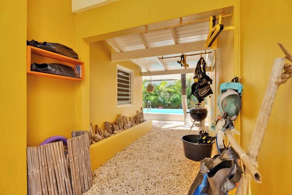 A hallway with a yellow wall, a wooden shoe rack, a grill, and a window leading to a pool. - Welcome to Kas Oranje, your island escape at Barefoot Apartments in Kralendijk, Bonaire.<br>This cozy one-bedroom studio offers authentic Caribbean charm, great value, and a peaceful location just a short walk from everything. (Kralendijk)