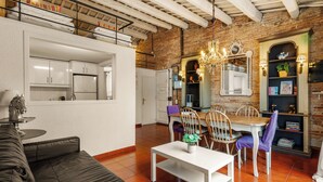 A modern apartment with a kitchen, dining area, and living room. It features exposed brick walls, white cabinetry, and a loft bedroom with a balcony. - Gràcia Loft + Terrace BBQ • AC & Fiber Wi-Fi (Barcelona)