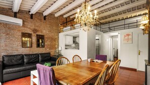 A spacious living area with a wooden dining table, leather sofa, and a chandelier. - Gràcia Loft + Terrace BBQ • AC & Fiber Wi-Fi (Barcelona)