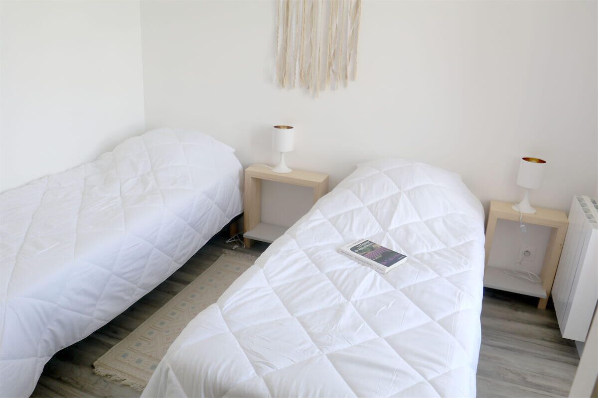 A bedroom with two single beds, each with a white duvet and a bedside table with a lamp.