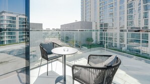 Un balcon moderne, doté de meubles en osier et d’une balustrade en verre, qui offre une vue sur le paysage urbain.