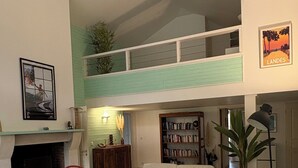 A spacious living room with a high ceiling, a fireplace, a bookshelf, and a large window. - Villa private heated pool, 4 bikes, nearby beach, surf 🌊 (Moliets-et-Maa)