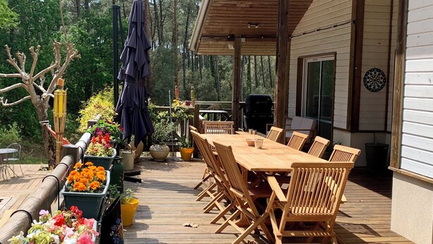 A wooden deck with a dining table and chairs, surrounded by potted plants and a covered area. - Villa private heated pool, 4 bikes, nearby beach, surf 🌊 (Moliets-et-Maa)