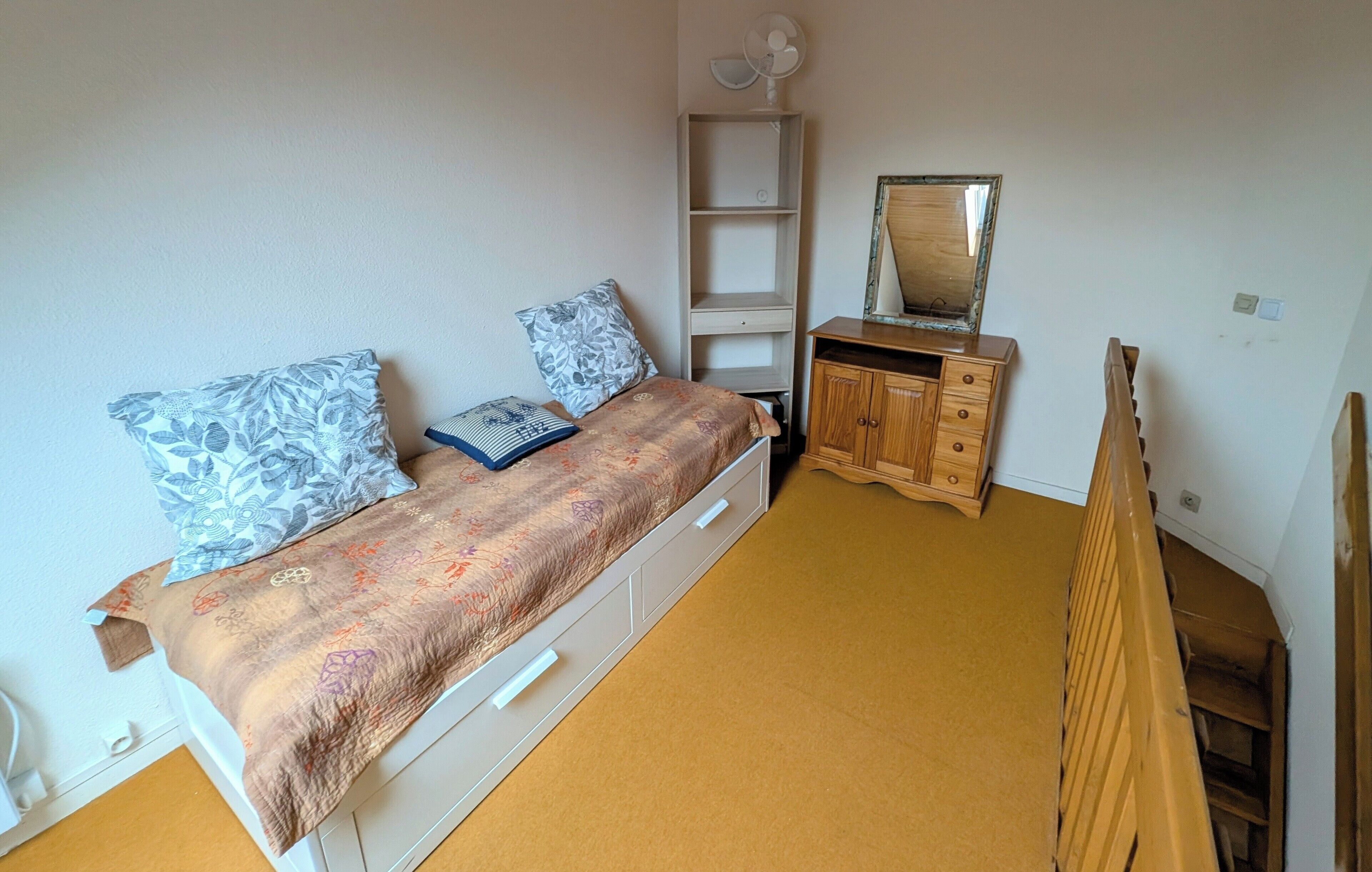 A bedroom with a bed, a wooden dresser, a mirror, and a white shelf unit.