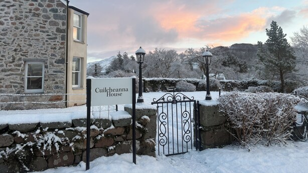 Un bâtiment en pierre avec une enseigne indiquant « Cuilcheanna House » et un portail recouvert de neige.