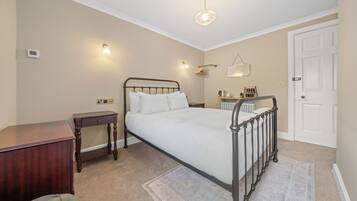 A bedroom with a bed, bedside table, nightstand, and a door.