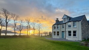 Une maison à deux étages avec une façade en pierre, de nombreuses fenêtres et une pelouse bien entretenue.